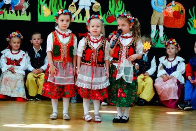 Trzy dziewczynki w strojach ludowych stoją na scenie i mówią do mikrofonu